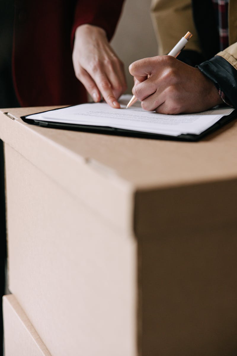 Hands signing lease documents on a cardboard box in an apartment.