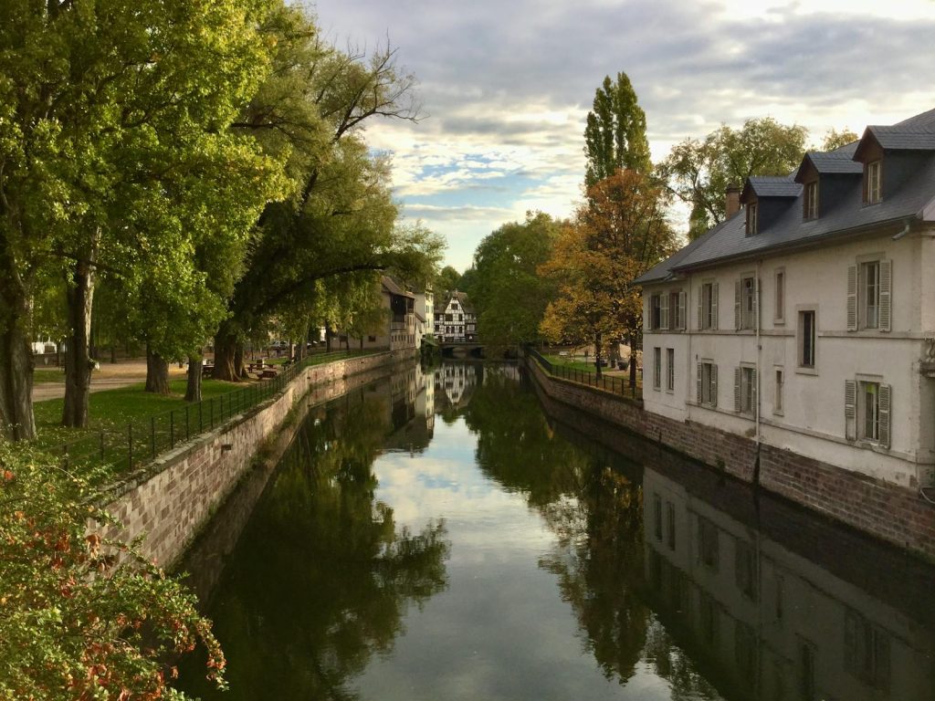 Peaceful autumn view of a canal in Strasbourg with traditional buildings and fall foliage reflections.